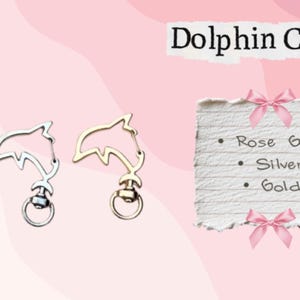 May include: Three dolphin-shaped clasps in rose gold, silver, and gold. The clasps have a ring at the bottom for attaching to items. The image includes text that says "Dolphin Clasp" and a list of the clasp colors.
