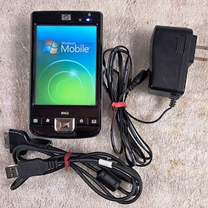 May include: Black HP iPAQ PDA with a Windows Mobile screen displaying a blue and green graphic. Includes a black charger, and a black USB cable. The PDA has the text "iPAQ" on the bottom.