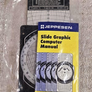 Puede incluir: Un manual Jeppesen Slide Graphic Computer con cubierta amarilla y una computadora de vuelo en blanco y negro con escalas de navegación circulares, cuadrículas de corrección de viento y texto instructivo, todo en una bolsa de plástico.