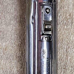 Puede incluir: Una linterna vintage de metal color plata con cuerpo cilíndrico y extremo redondeado. La cabeza presenta el logotipo de Ray-O-Vac y el lateral está grabado con el texto PROPERTY OF GREAT LAKES STEEL CORP, incluyendo un interruptor deslizante.
