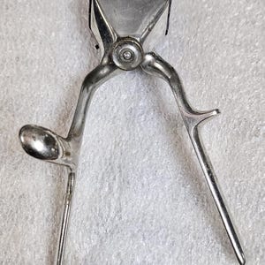 Puede incluir: Una cortadora de pelo manual vintage fabricada en metal pulido de tono plateado. La herramienta presenta un conjunto de cuchillas negras en forma de peine en la parte superior, un tornillo de pivote central y dos mangos largos y delgados.