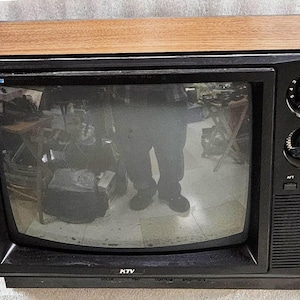 Puede incluir: Un televisor KTV vintage con una carcasa superior de imitación madera y un marco frontal negro. La unidad incluye dos grandes perillas circulares en el lado derecho para la selección de canales y el control de volumen, junto a una rejilla.