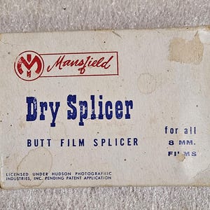 May include: A vintage Mansfield Dry Splicer box for 8mm films. The box is off-white with red and blue text. The text includes "Mansfield", "Dry Splicer", and "Butt Film Splicer". The box is slightly worn.