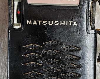 May include: A black leather-cased Matsushita portable radio featuring a rectangular frequency dial with numbers 54, 6, 7, 9, 12, 16. The front panel displays a diamond-shaped perforated speaker grille pattern and a side-mounted tuning wheel.