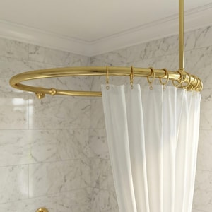 Puede incluir: Una barra de cortina de ducha dorada, de forma ovalada, suspendida del techo. La barra está sujeta a un soporte vertical. Una cortina de ducha blanca cuelga de la barra, con anillos dorados. El fondo es una pared de azulejos de mármol.