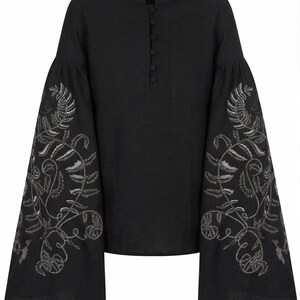 May include: Black linen blouse with long, flared sleeves. The sleeves are adorned with intricate silver embroidery featuring a botanical design. The blouse has a mandarin collar and a button-down front.