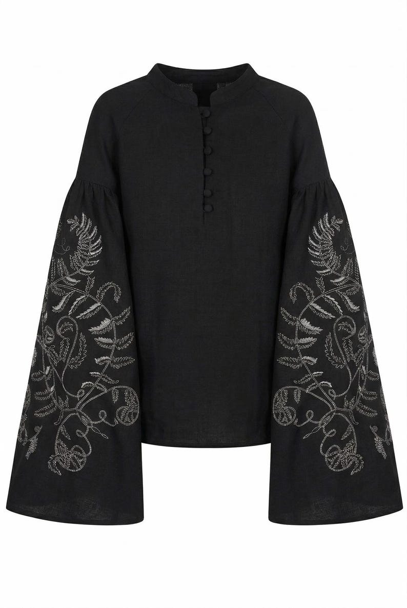 May include: Black linen blouse with long, flared sleeves. The sleeves are adorned with intricate silver embroidery featuring a botanical design. The blouse has a mandarin collar and a button-down front.