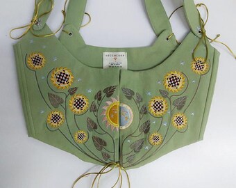 May include: A sage green corset top featuring embroidered sunflowers with checkered centers and a central sun and moon motif. The garment includes thin gold ribbon ties at the shoulders and front hem, with a Hrushenka brand label visible at the neckline.