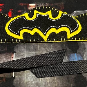 May include: Black Batman-themed headband with yellow stitching and a yellow Batman logo. The name "Steven" is embroidered in yellow. The headband has a black strap for securing it.