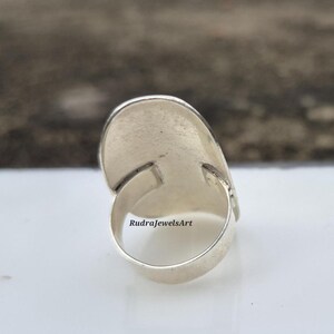 May include: A silver ring with an oval-shaped, light-colored stone. The ring band is smooth and rounded, and the stone setting is rectangular. The text "RudraJewelsArt" is visible on the ring.