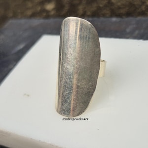 May include: A silver-toned ring with a long, curved design. The ring has a smooth, polished surface with a slight texture. The ring is a statement piece, perfect for adding a touch of modern style to any outfit.