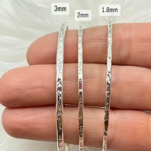 May include: Three silver hammered bangles of varying widths: 3mm, 2mm, and 1.8mm. The bangles have a textured finish and are shown close-up. The image displays the different sizes available.