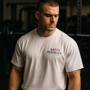May include: A white crew neck t-shirt with the text "NATTY MENTALITY" in red and black. The shirt also has the text "NO RACKS JUST WORK" in black. The person in the image is wearing the shirt.