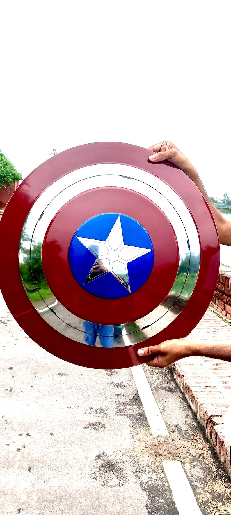 Op de afbeelding: Een Captain America-schild, met een rode buitenring, een zilveren binnenring en een blauw midden met een witte ster. Het schild wordt door twee handen vastgehouden.