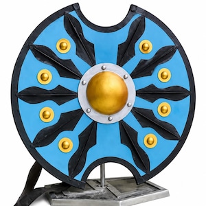 Op de afbeelding: Een cirkelvormig schild met een felblauwe basis, zwarte radiale accenten en goudkleurige ronde noppen. Het midden heeft een prominente gouden koepel omringd door een zilveren ring met klinknagels. Het schild staat op een zilverkleurige metalen standaard.