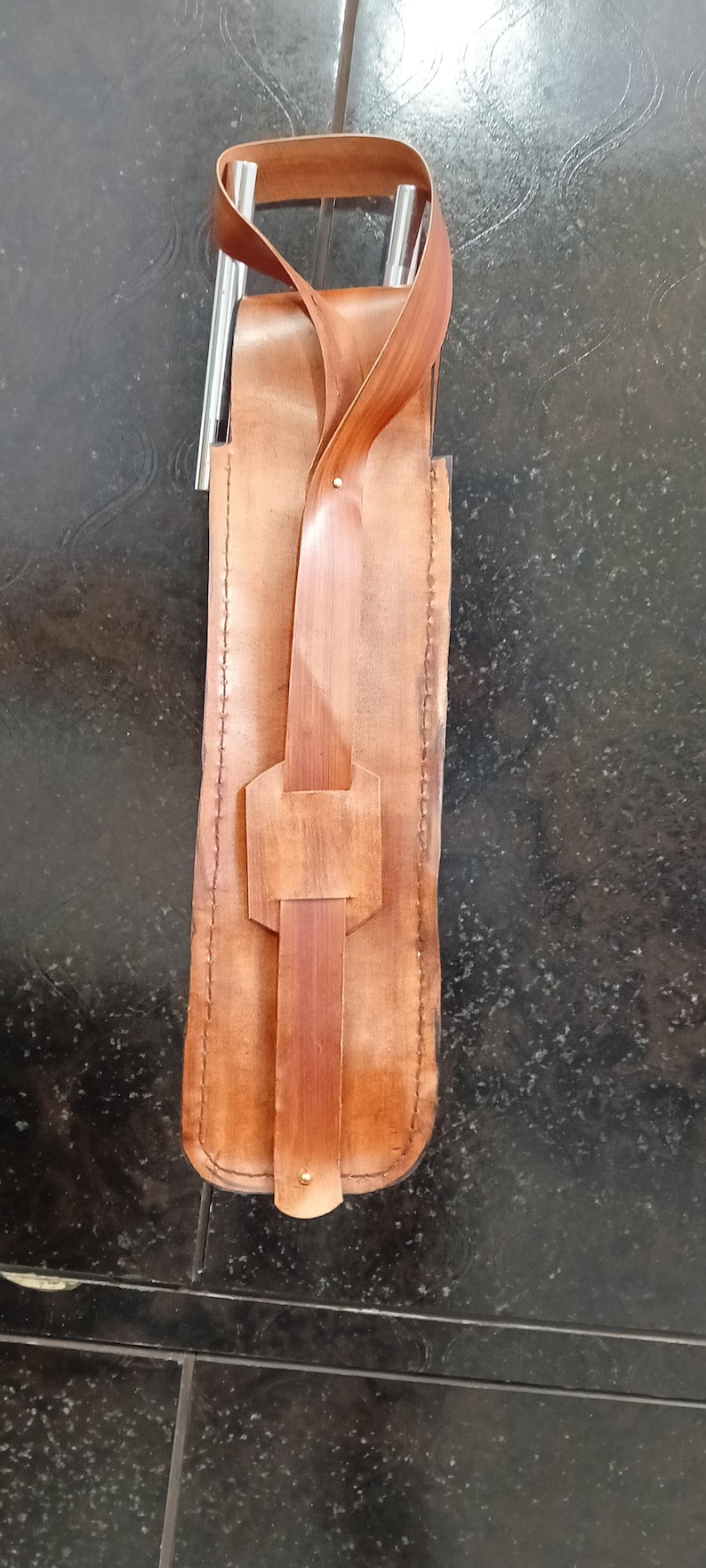 Peut inclure: Un &eacute;tui &agrave; couteau en cuir fait &agrave; la main, de couleur marron clair, avec un design unique. Il est dot&eacute; d'une fermeture &agrave; sangle et boucle, et d'un manche en bois brun plus fonc&eacute;. L'&eacute;tui est con&ccedil;u pour contenir un couteau.