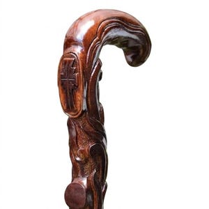 Pode incluir: Uma bengala de madeira castanho-escura com acabamento polido e um cabo curvo ornamentado. O cabo é esculpido de forma intrincada com padrões em espiral e um símbolo de cruz proeminente gravado na lateral, exibindo um trabalho detalhado.