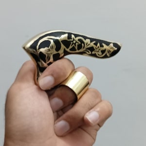 Pu&ograve; includere: Un anello color oro e un manico nero e oro con disegni floreali. Il manico &egrave; tenuto in una mano e l'anello &egrave; su un dito. Il manico sembra far parte di un bastone da passeggio.