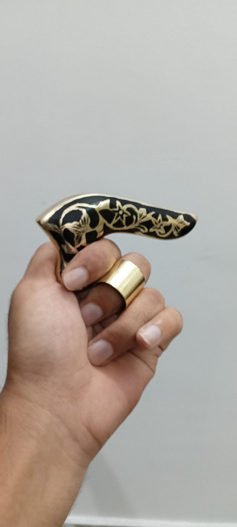 Pu&ograve; includere: Un anello color oro e un manico nero e oro con disegni floreali. Il manico &egrave; tenuto in una mano e l'anello &egrave; su un dito. Il manico sembra far parte di un bastone da passeggio.
