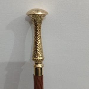 Peut inclure: Canne de marche d&eacute;corative avec une poign&eacute;e dor&eacute;e orn&eacute;e et un f&ucirc;t en bois brun fonc&eacute;. La poign&eacute;e pr&eacute;sente un dessus arrondi et des sculptures d&eacute;taill&eacute;es. La tige a des incrustations.