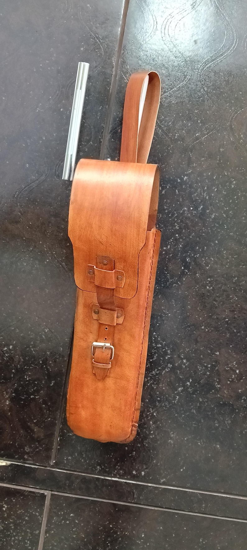 Peut inclure: Un &eacute;tui en cuir marron fait &agrave; la main avec une fermeture &agrave; boucle et une poign&eacute;e. L'&eacute;tui est con&ccedil;u pour contenir un objet long et fin, peut-&ecirc;tre un outil ou un ustensile. Une tige m&eacute;tallique argent&eacute;e est &agrave; c&ocirc;t&eacute; de l'&eacute;tui.