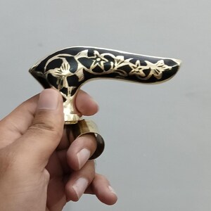 Pu&ograve; includere: Maniglia in ottone ornata con un motivo floreale nero. La maniglia presenta una forma curva e un anello per un dito. Il design &egrave; probabilmente per un bastone o un bastone da passeggio.