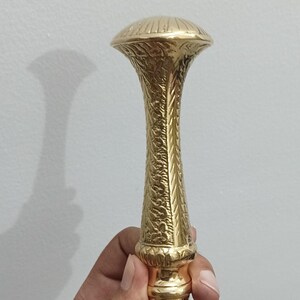 Peut inclure: Une poign&eacute;e de canne dor&eacute;e avec un motif orn&eacute; et textur&eacute;. La poign&eacute;e a un dessus en forme de champignon et une tige d&eacute;taill&eacute;e et &agrave; motifs. La base est de couleur or contrastante, et la canne semble &ecirc;tre en bois.