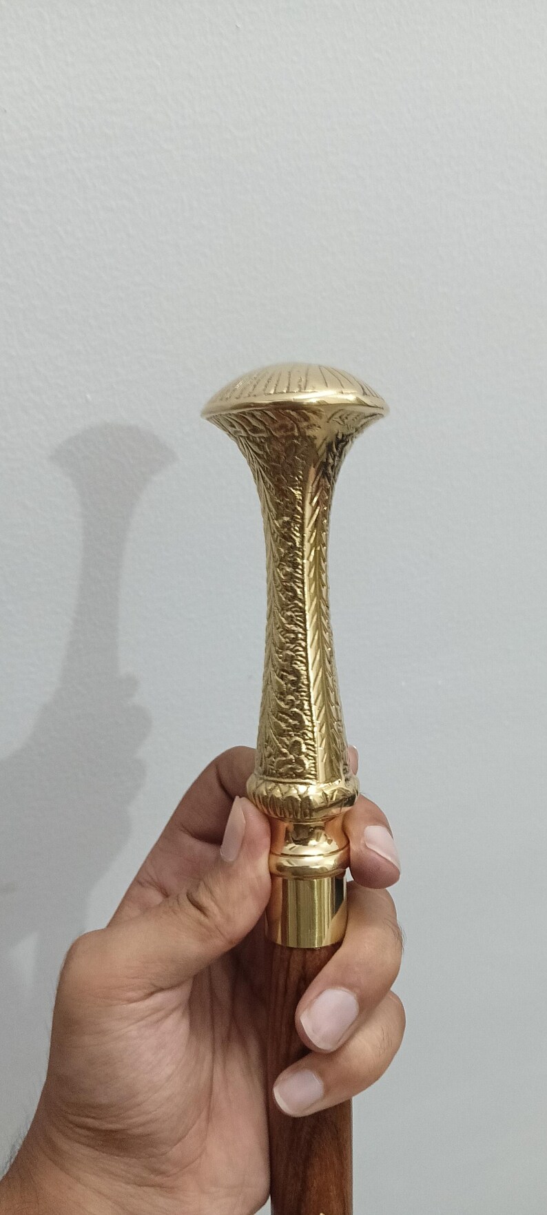 Peut inclure: Une poign&eacute;e de canne dor&eacute;e avec un motif orn&eacute; et textur&eacute;. La poign&eacute;e a un dessus en forme de champignon et une tige d&eacute;taill&eacute;e et &agrave; motifs. La base est de couleur or contrastante, et la canne semble &ecirc;tre en bois.