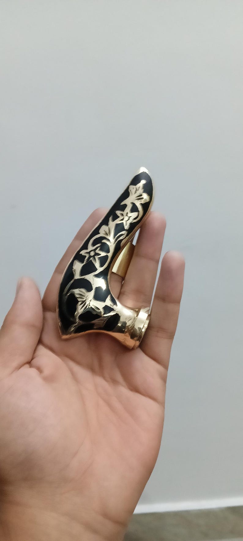 Pu&ograve; includere: Un oggetto curvo color oro con una parte superiore nera a motivi floreali. L'oggetto ha una base ad anello ed &egrave; tenuto in mano. Il design presenta accenti floreali color oro su sfondo nero.