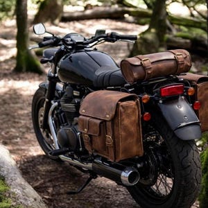 May include: A black motorcycle equipped with brown leather saddlebags and a matching cylindrical leather roll bag attached to the rear. The motorcycle features a black fuel tank, a chrome exhaust pipe, and black spoked wheels with rubber tires.