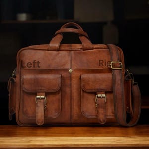 May include: A brown leather briefcase with two front pockets, each secured by a metal buckle. The bag has a top handle and a detachable shoulder strap. The word "Left" is printed on the left side of the bag, and the word "Right" is printed on the right side.