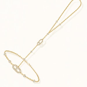 May include: A gold hand chain bracelet featuring a delicate chain adorned with small round clear stones. The design includes two oval-shaped links encrusted with clear stones, one positioned on the wrist section and one on the finger loop.