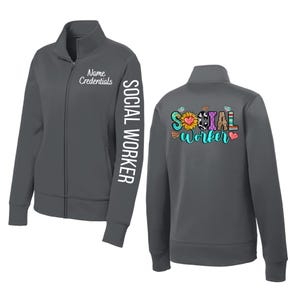 May include: A charcoal gray zip-up jacket with the words "SOCIAL WORKER" printed vertically on the left sleeve. The front of the jacket has the text "Name Credentials" in white. The back of the jacket features the words "SOCIAL WORKER" in a colorful design.