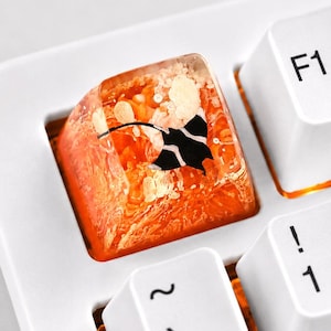 May include: A custom translucent orange resin keycap featuring an embedded black stingray silhouette and white textured inclusions, installed on a white mechanical keyboard next to standard white keys labeled F1, F2, 1, 2, and the tilde symbol.