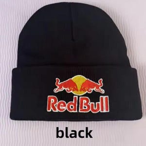 Può includere: Berretto nero con il logo Red Bull ricamato in rosso e bianco. Il logo mostra due tori rossi che si fronteggiano su un cerchio giallo. Le parole "Red Bull" sono ricamate sotto. La parola "black" è stampata in basso.