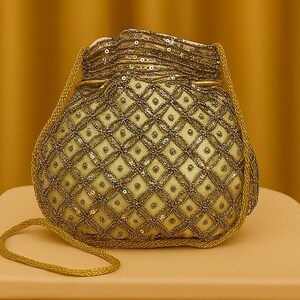 Könnte beinhalten: Eine goldfarbene, mit Perlen besetzte Beuteltasche mit Kordelzug, die auf einem kleinen, hellfarbigen Tisch liegt. Die Tasche hat ein Rautenmuster und ist mit Pailletten verziert. Der Text "NIYA TRENDS" ist darunter zu sehen.
