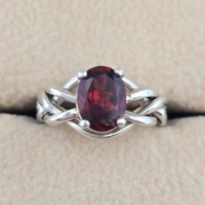May include: A silver ring with a red oval gemstone set in a braided band.