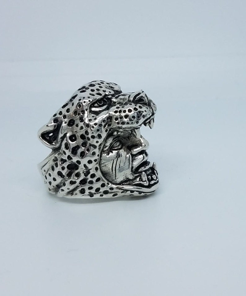 May include: A silver ring with a detailed design of a leopard's head. The leopard's mouth is open, revealing sharp teeth.