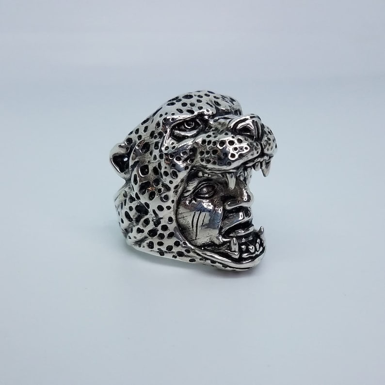 May include: A silver ring with a detailed design of a cheetah's head with an open mouth. The cheetah's fur is textured with spots.