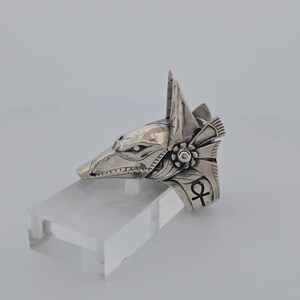 May include: Silver ring featuring an Anubis head design with intricate details. The ring also includes an ankh symbol.