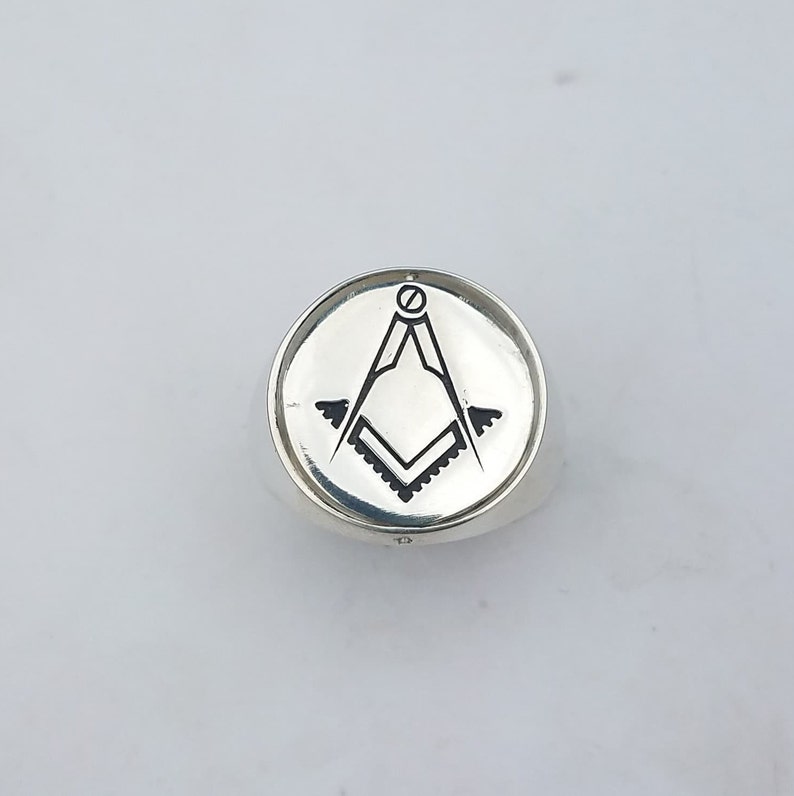 K&ouml;nnte beinhalten: Ein silberner Ring mit einem schwarz-wei&szlig;en freimaurerischen Symbol, das auf der Oberseite graviert ist.