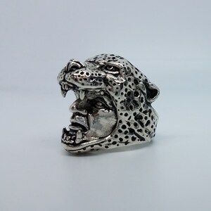 May include: A silver ring with a detailed design of a leopard's head with an open mouth.