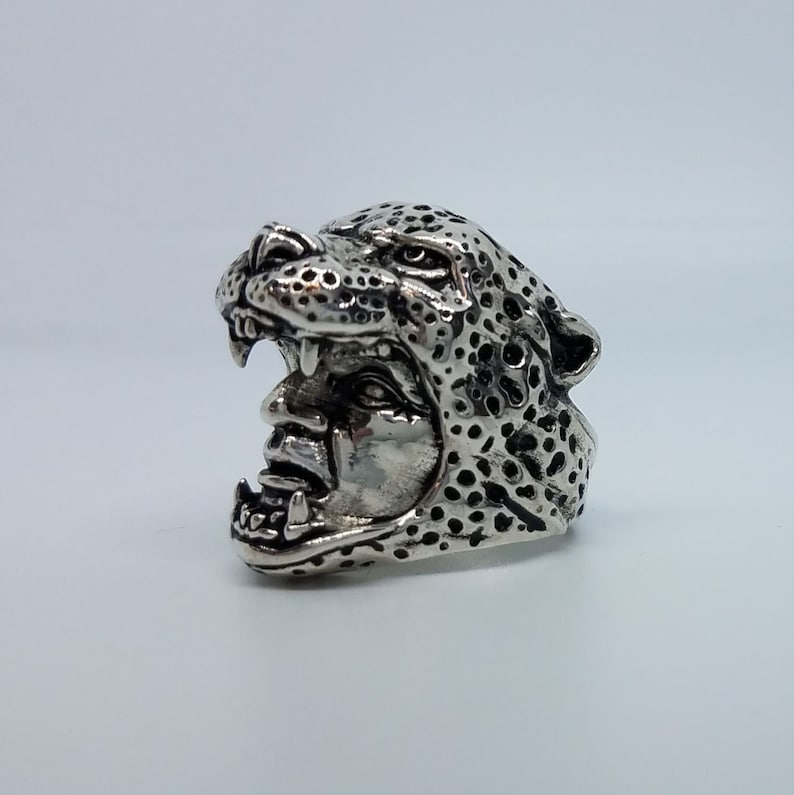 May include: A silver ring with a detailed design of a leopard's head with an open mouth.