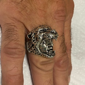May include: A silver ring with a detailed design of a leopard's head with an open mouth.