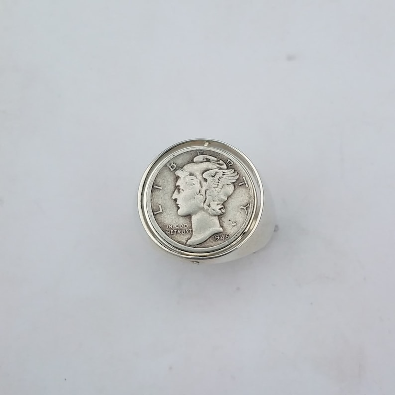 K&ouml;nnte beinhalten: Silberring mit einer 1945 Walking Liberty-Halbdollar-M&uuml;nze. Die M&uuml;nze ist in einer Zargenfassung gefasst und der Ring ist poliert.