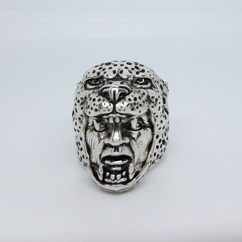 May include: A silver ring with a detailed design of a leopard's face. The ring features a realistic depiction of the animal's features, including its spots, eyes, and teeth.