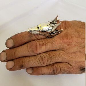 May include: A silver ring with a detailed wolf head design. The ring is worn on a finger.
