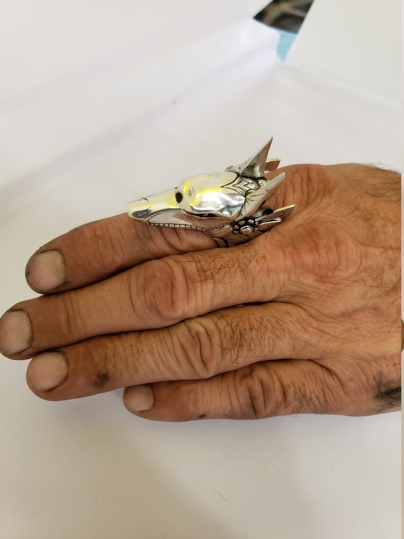 May include: A silver ring with a detailed wolf head design. The ring is worn on a finger.