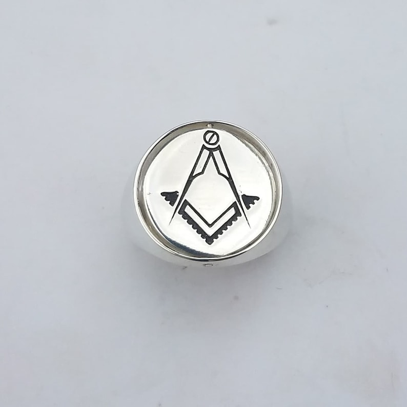 K&ouml;nnte beinhalten: Ein silberner Ring mit einem schwarz-wei&szlig;en freimaurerischen Symbol, das auf der Oberseite graviert ist.