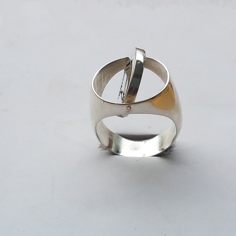 K&ouml;nnte beinhalten: Ein silberner Ring mit einem drehbaren, kreisf&ouml;rmigen Design. Der Ring ist aus Metall gefertigt und hat eine glatte, polierte Oberfl&auml;che.